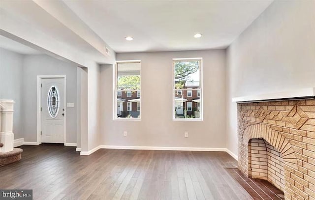 unfurnished living room with dark wood finished floors, baseboards, and a brick fireplace