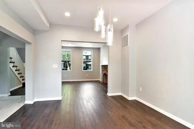 unfurnished living room with stairs, a chandelier, dark wood-type flooring, baseboards, and a fireplace