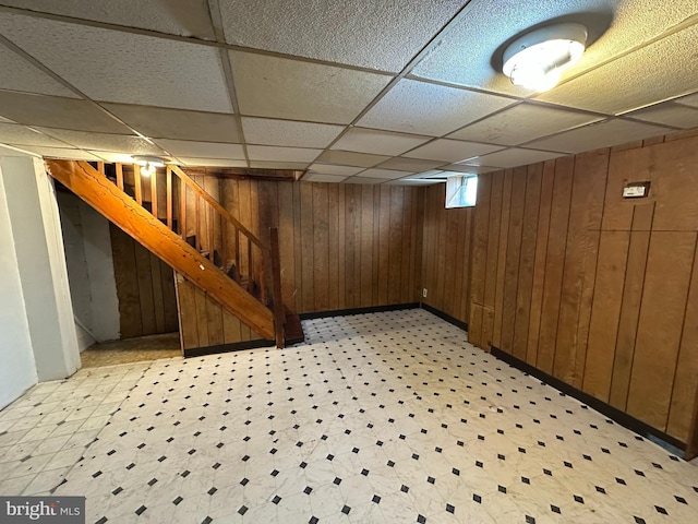 below grade area featuring stairs, wood walls, light floors, and a paneled ceiling
