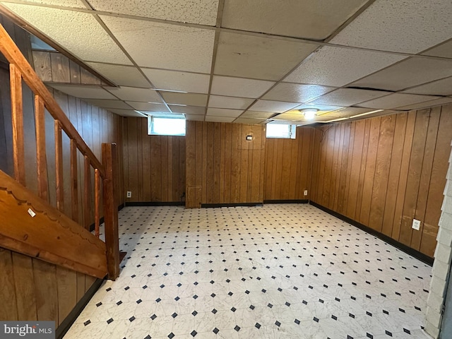 basement with wooden walls, stairway, and a paneled ceiling