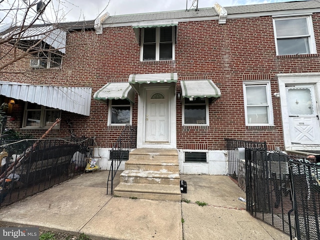 townhome / multi-family property with brick siding, fence, and roof with shingles