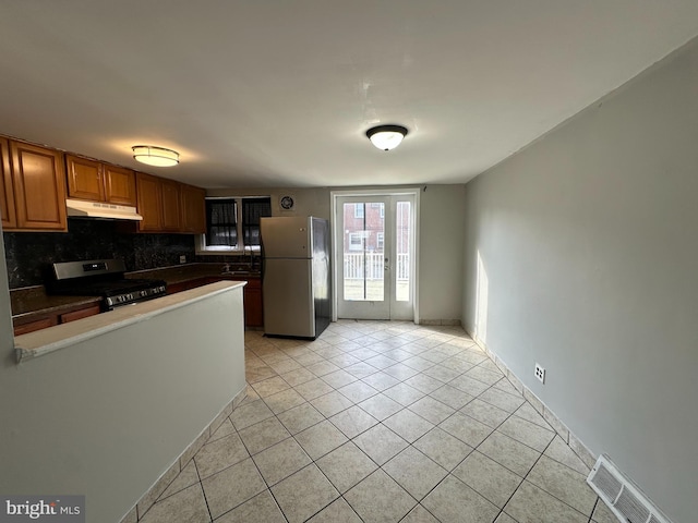 kitchen featuring light tile patterned flooring, decorative backsplash, visible vents, stainless steel appliances, and under cabinet range hood