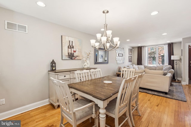 dining area with light wood-type flooring, baseboards, visible vents, and a notable chandelier