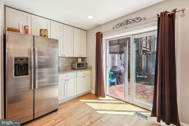 kitchen featuring white cabinetry, stainless steel fridge with ice dispenser, backsplash, and light wood finished floors