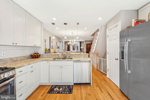 kitchen with a chandelier, a peninsula, appliances with stainless steel finishes, white cabinetry, and a sink