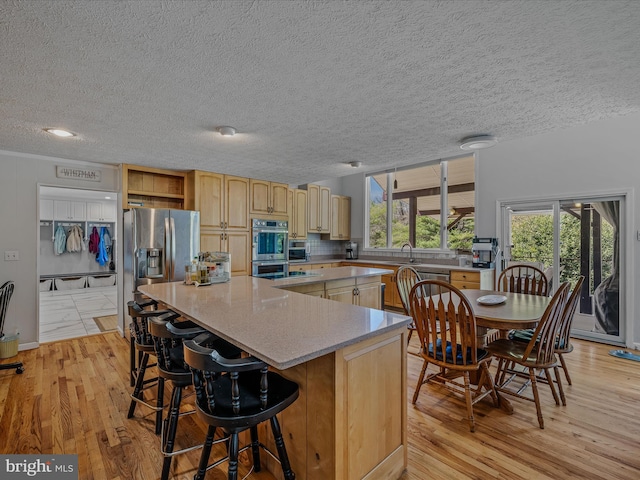 kitchen with light wood-style flooring, a textured ceiling, appliances with stainless steel finishes, and a spacious island
