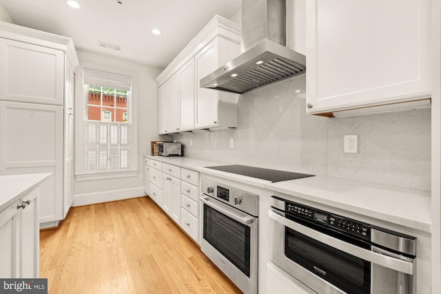 808 Cameron St, Alexandria, VA 22314 - kitchen featuring wall chimney exhaust hood, stainless steel oven, oven, light wood-style flooring, and white cabinets