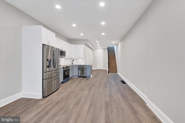 kitchen featuring white cabinets, light countertops, light wood finished floors, stainless steel appliances, and tasteful backsplash
