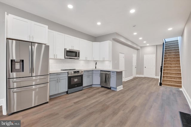 kitchen with light countertops, appliances with stainless steel finishes, light wood-type flooring, gray cabinetry, and backsplash