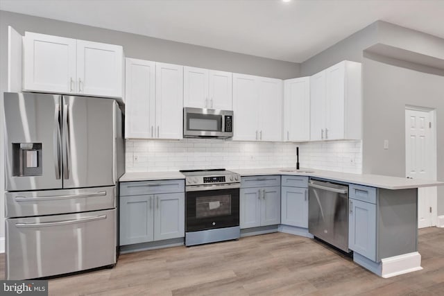 kitchen with light countertops, decorative backsplash, a sink, light wood finished floors, and appliances with stainless steel finishes