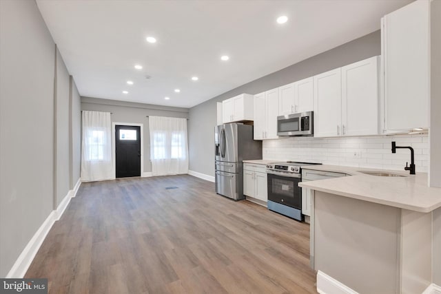 kitchen with a sink, tasteful backsplash, light stone countertops, light wood-style flooring, and stainless steel appliances