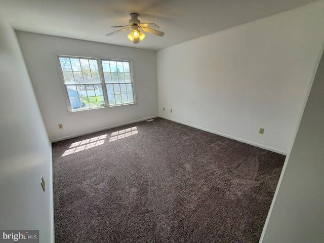 empty room featuring dark colored carpet, baseboards, and ceiling fan