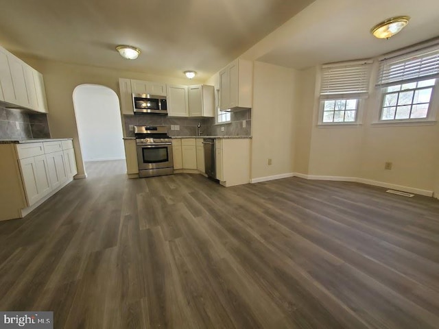 kitchen with appliances with stainless steel finishes, arched walkways, tasteful backsplash, visible vents, and dark wood-style floors