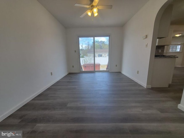unfurnished room featuring arched walkways, ceiling fan, baseboards, and dark wood-style floors