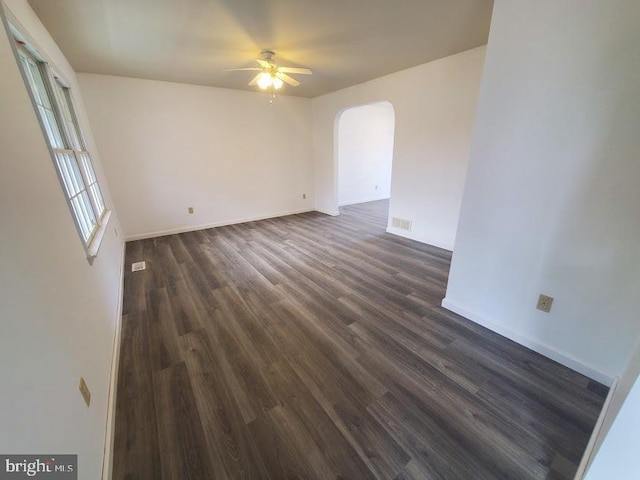 spare room featuring a ceiling fan, visible vents, arched walkways, baseboards, and dark wood-type flooring