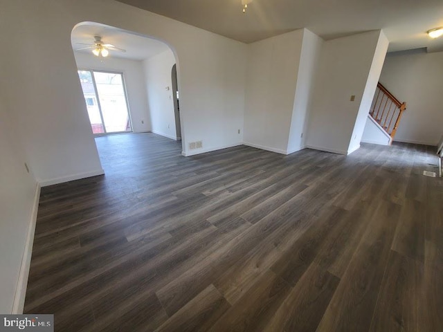 unfurnished room with dark wood-type flooring, arched walkways, stairs, and a ceiling fan