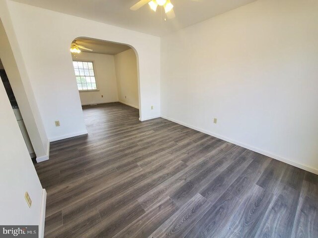 empty room featuring arched walkways, ceiling fan, baseboards, and dark wood-type flooring