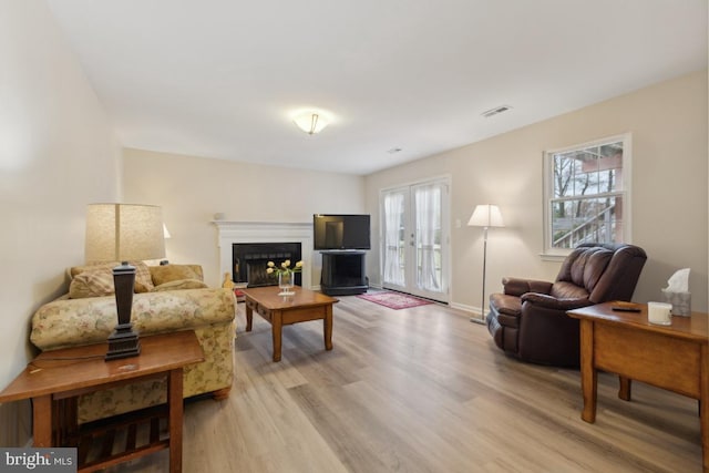 living room featuring light wood-style flooring, a fireplace, and visible vents