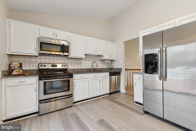 kitchen featuring tasteful backsplash, vaulted ceiling, stainless steel appliances, light wood-style floors, and white cabinets
