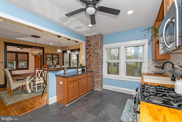 kitchen featuring stainless steel appliances, a sink, decorative light fixtures, brown cabinetry, and ceiling fan with notable chandelier