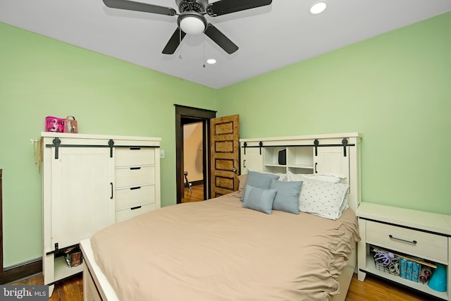 bedroom with wood finished floors, recessed lighting, ceiling fan, and a barn door