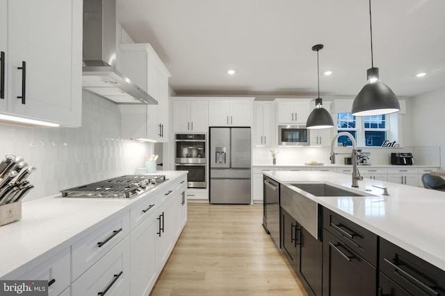 kitchen featuring wall chimney range hood, white cabinets, light countertops, a sink, and stainless steel appliances