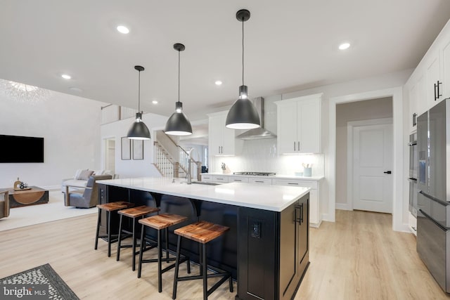 kitchen with gas stovetop, ventilation hood, light countertops, a sink, and light wood finished floors