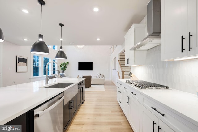 kitchen featuring wall chimney range hood, stainless steel appliances, white cabinets, and light countertops