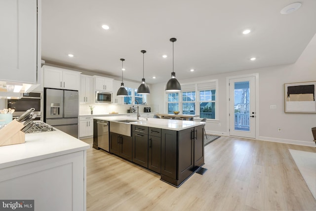 kitchen with light wood-style flooring, white cabinets, appliances with stainless steel finishes, light countertops, and a sink