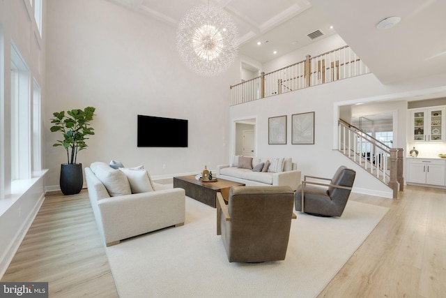 living area featuring visible vents, baseboards, an inviting chandelier, light wood-type flooring, and stairs