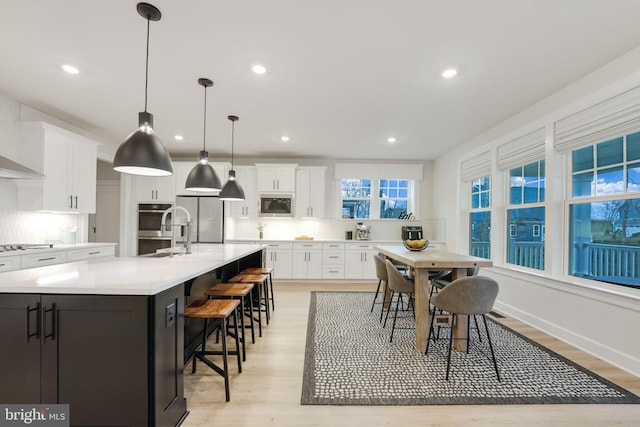 kitchen featuring light countertops, white cabinetry, backsplash, appliances with stainless steel finishes, and light wood finished floors