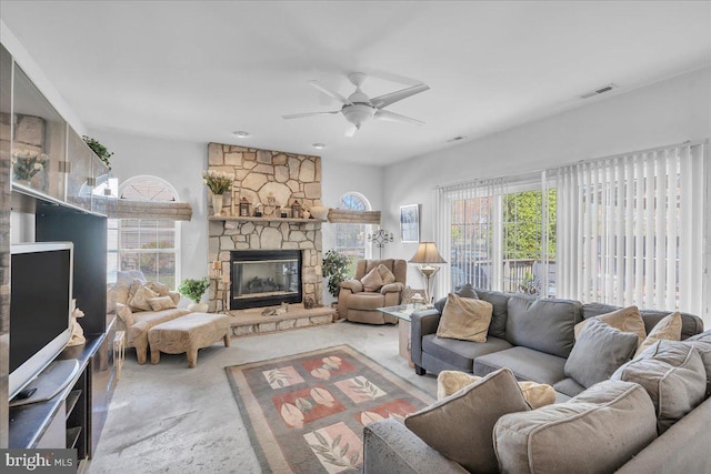 carpeted living area with visible vents, a healthy amount of sunlight, ceiling fan, and a stone fireplace