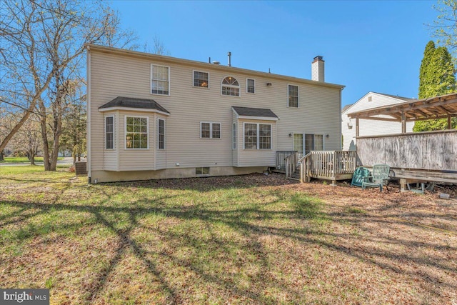 back of house with a pergola, a wooden deck, a lawn, and a chimney