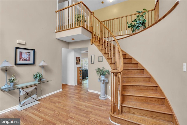 stairs featuring a towering ceiling, baseboards, and wood finished floors