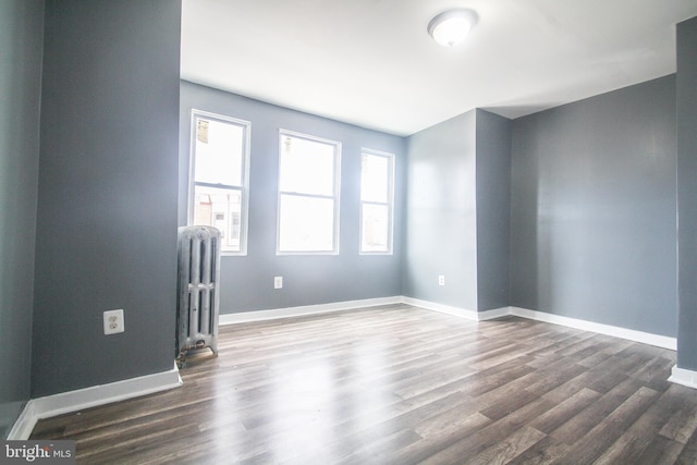 empty room featuring baseboards, radiator heating unit, and dark wood-type flooring