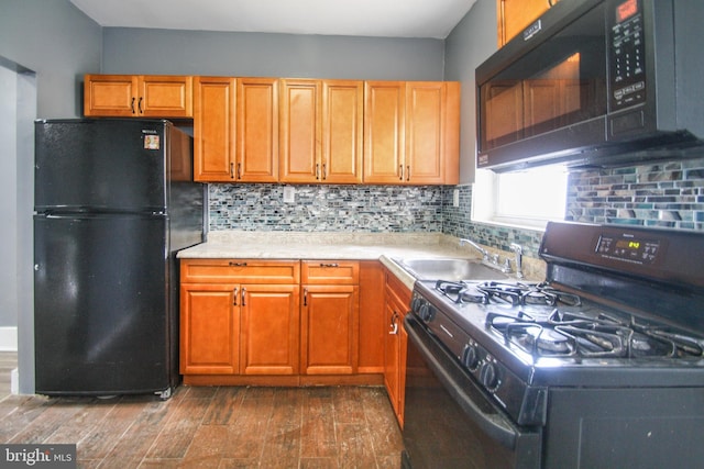 kitchen featuring a sink, backsplash, light countertops, dark wood-type flooring, and black appliances
