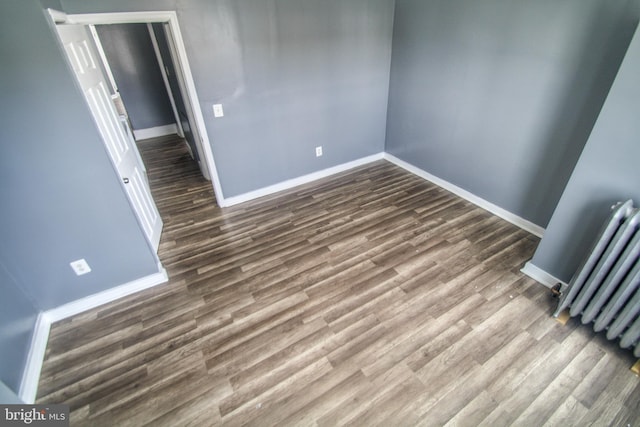 spare room with baseboards, dark wood-style floors, and radiator