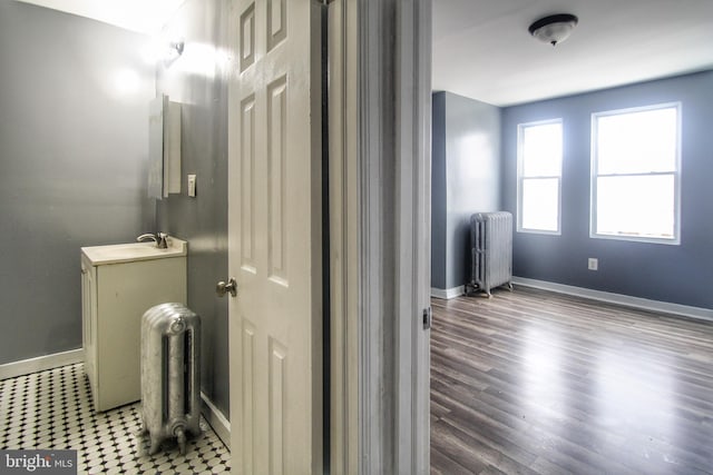 bathroom featuring wood finished floors, baseboards, vanity, and radiator