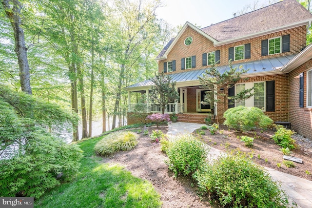 view of front of home featuring a standing seam roof, a shingled roof, a porch, and brick siding