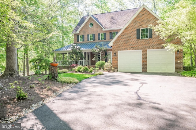 view of front of property featuring an attached garage, brick siding, a standing seam roof, covered porch, and driveway