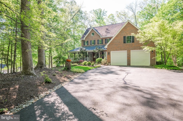 view of front facade featuring covered porch, a standing seam roof, driveway, a garage, and brick siding