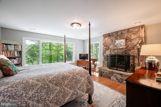 bedroom featuring visible vents, a fireplace, wood finished floors, and multiple windows