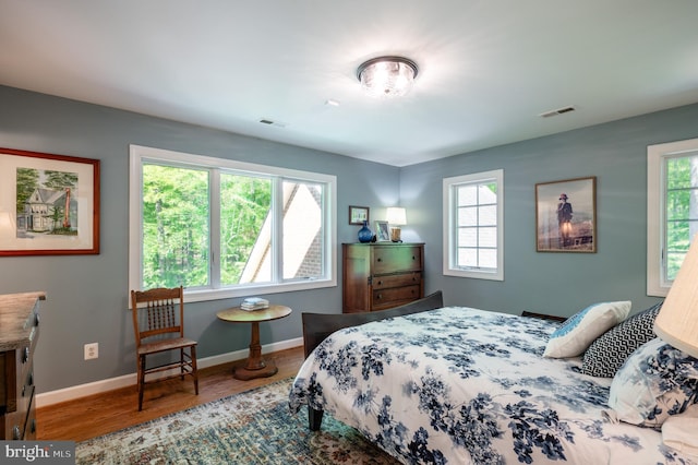 bedroom featuring visible vents, baseboards, wood finished floors, and multiple windows
