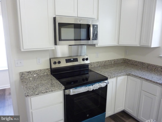 kitchen with dark wood-style flooring, white cabinetry, light stone counters, and appliances with stainless steel finishes