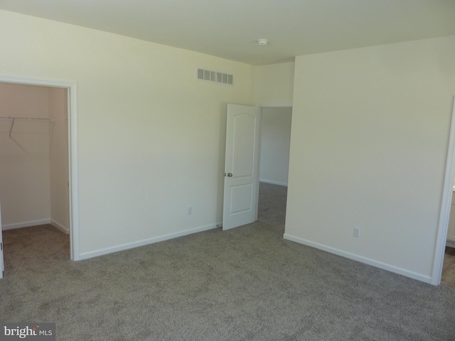 unfurnished bedroom featuring a closet, visible vents, carpet flooring, and a walk in closet