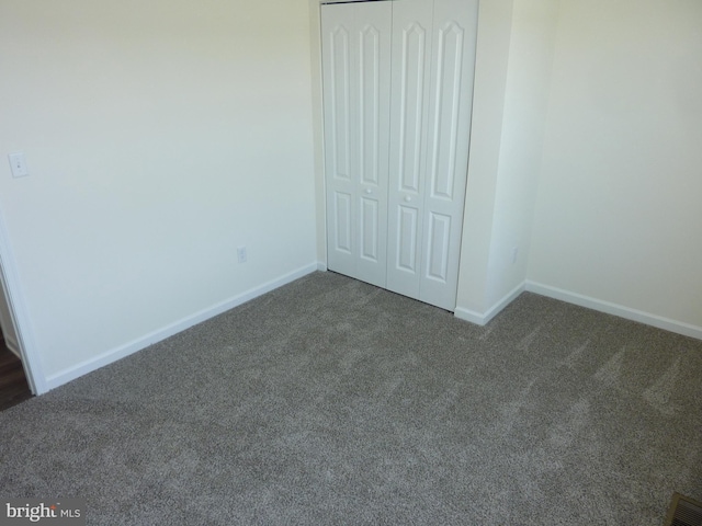 unfurnished bedroom with a closet, baseboards, dark colored carpet, and visible vents