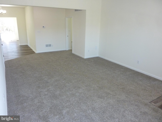carpeted spare room with a chandelier, visible vents, and baseboards
