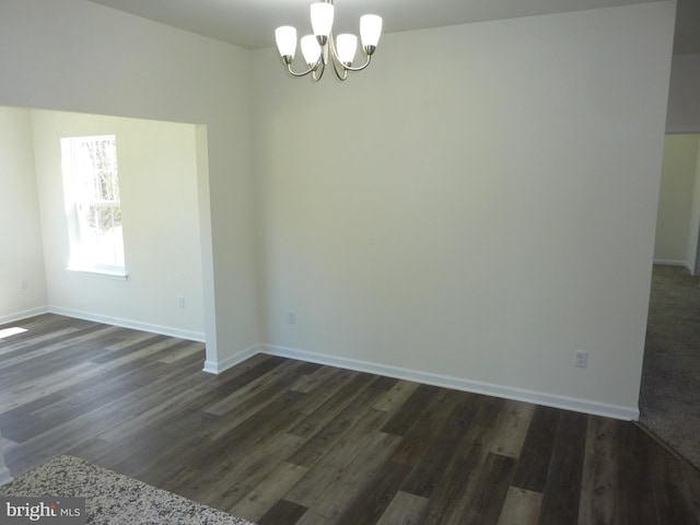 empty room with a chandelier, baseboards, and dark wood finished floors