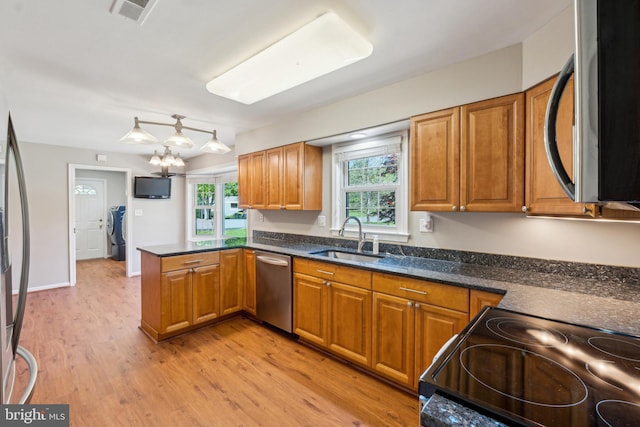 kitchen with appliances with stainless steel finishes, brown cabinets, a sink, a peninsula, and light wood-style flooring