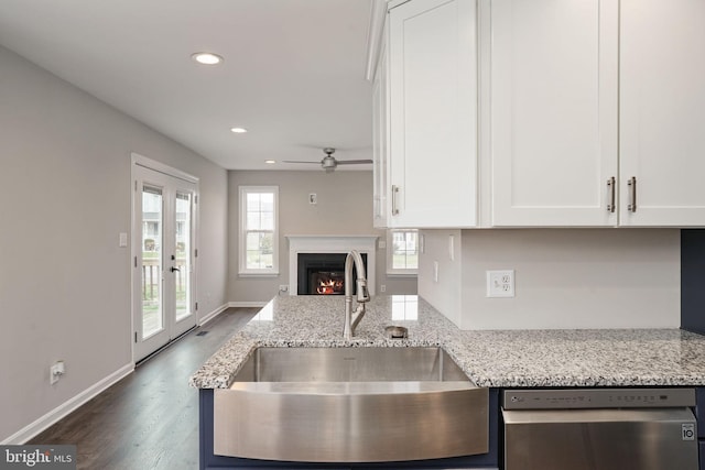 kitchen featuring stainless steel dishwasher, white cabinetry, a lit fireplace, and a sink